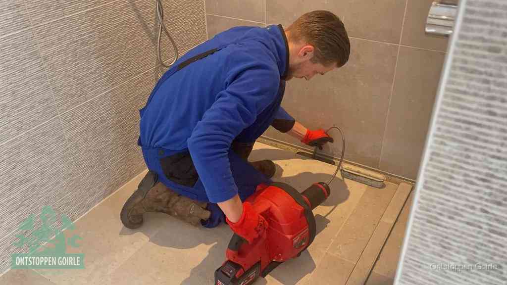 Een monteur ontstopt een langwerpige douchegoot met een elektrische veer, een doucheputje verstopt door haren en zeep in Goirle