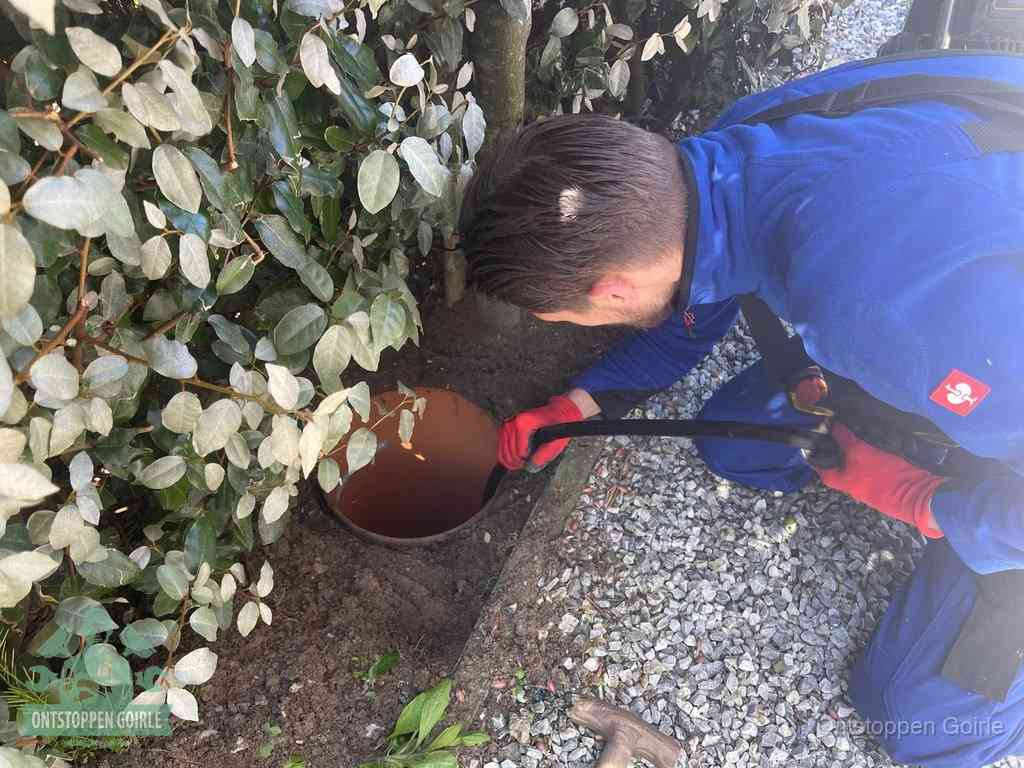 Een monteur voert een slang in een geopende rioolput in de tuin om het hoofdriool te ontstoppen in Goirle